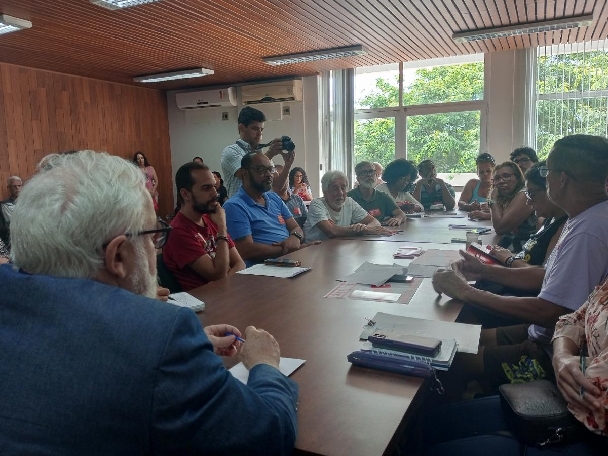 Pessoas presentes na reunião, sentadas em volta de uma mesa de madeira