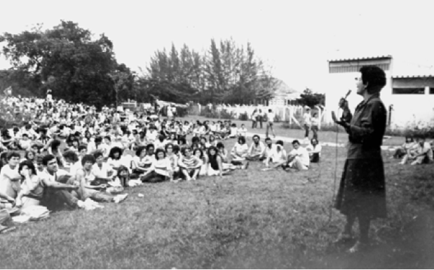 Foto em preto e branco com a professora Marilena Chauí em pé, à direita, e estudantes sentados no gramado em frente.
