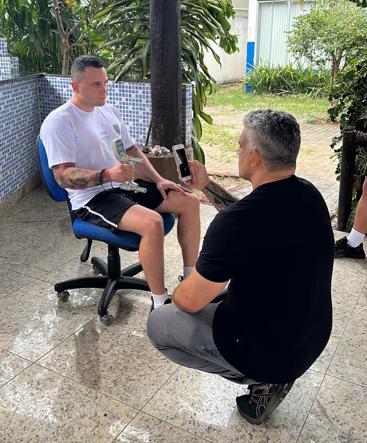 Pesquisador agachado avalia um policial sentado usando o equipamento handgrip.