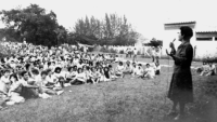 Foto em preto e branco com a professora Marilena Chauí em pé, à direita, e estudantes sentados no gramado em frente.