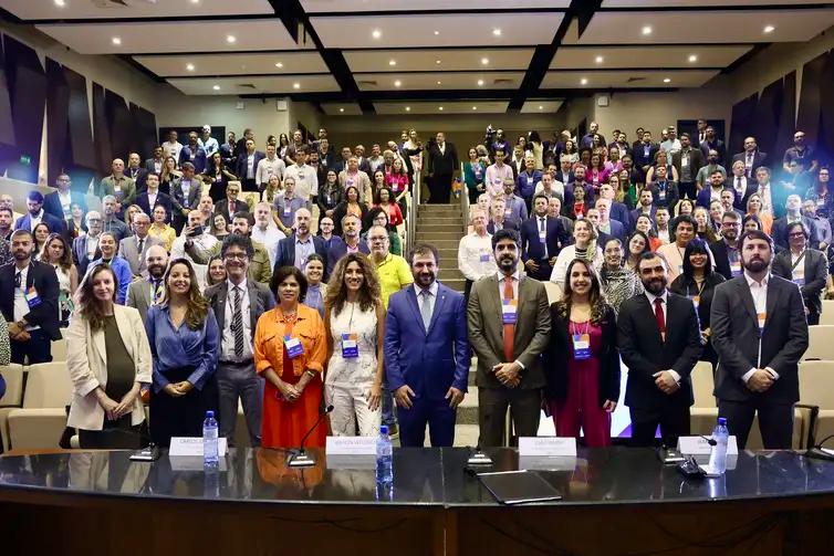 Foto do auditório com todos os presentes (à frente, a mesa principal de abertura e, atrás, os participantes)