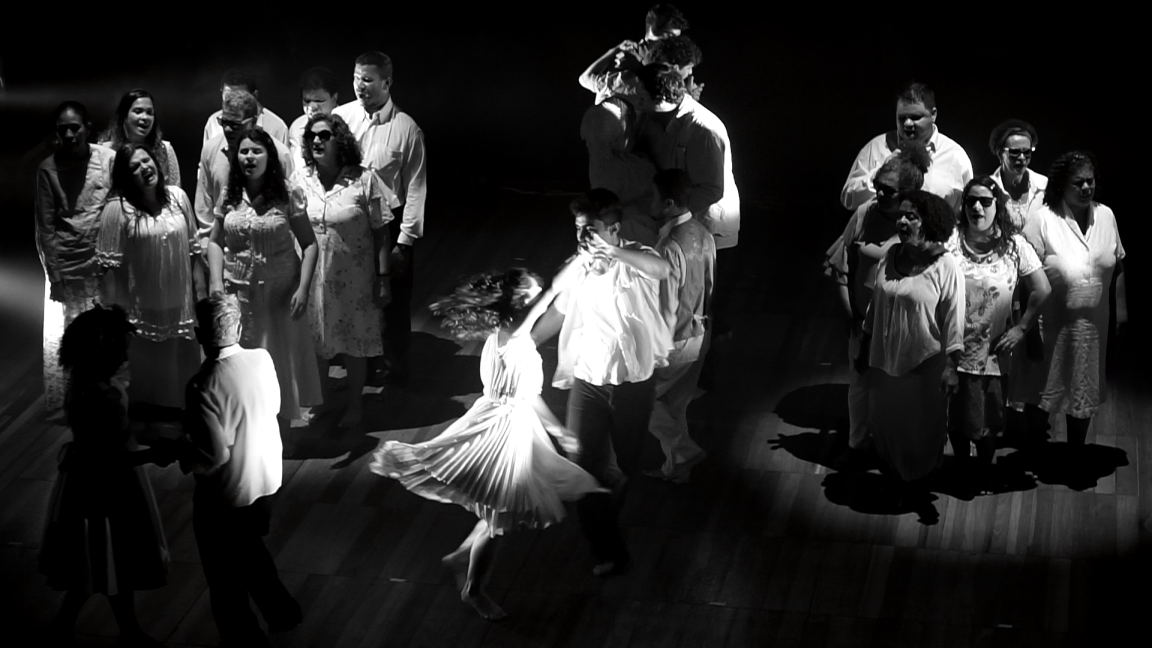 Foto dos cantores em volta de um casal que dança no centro do palco, com a moça rodopiando