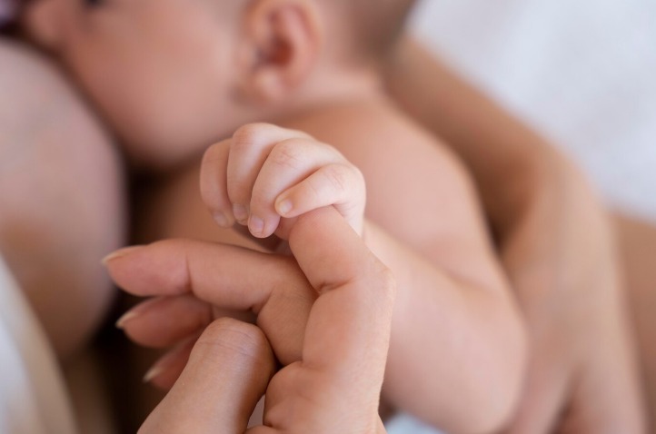 Imagem de um bebê sendo amamentado, segurando no dedo da mãe