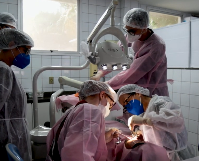 Imagem de estudantes de Odontologia em um consultório, observando a boca de um paciente