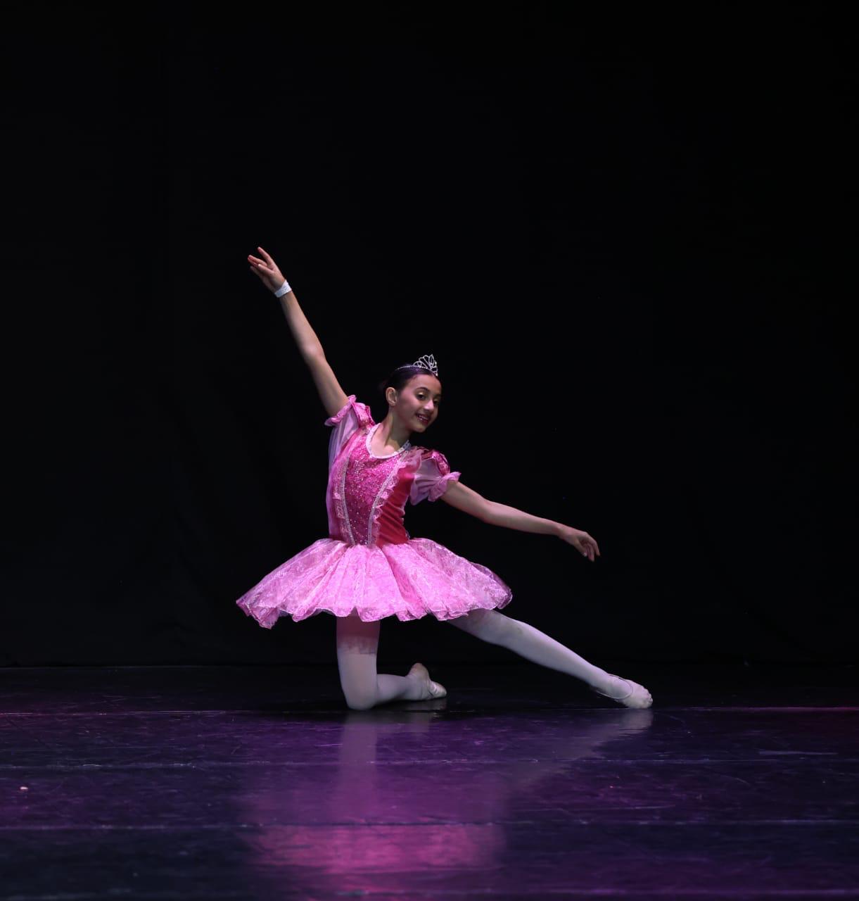 Foto de uma bailarina com roupa rosa dançando no palco