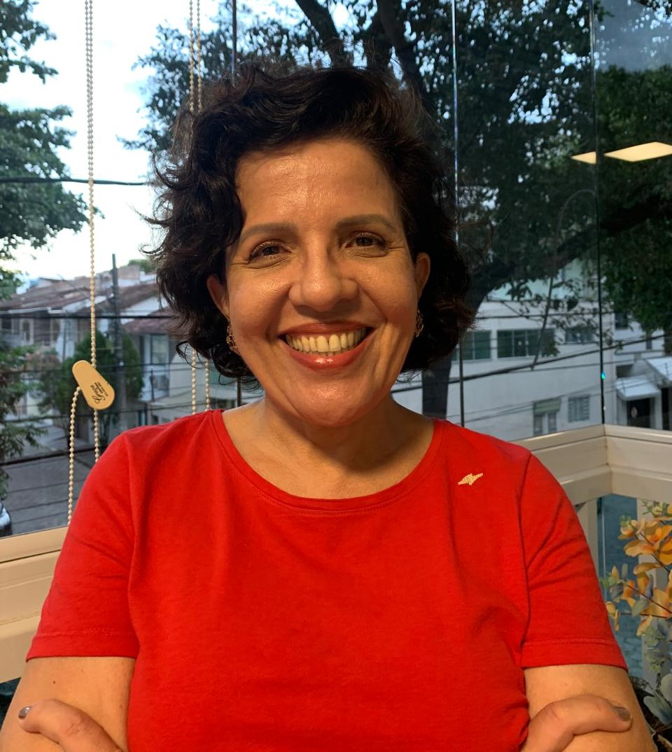 Foto da professora Adriana Campos, sorrindo para a câmera e de braços cruzados.