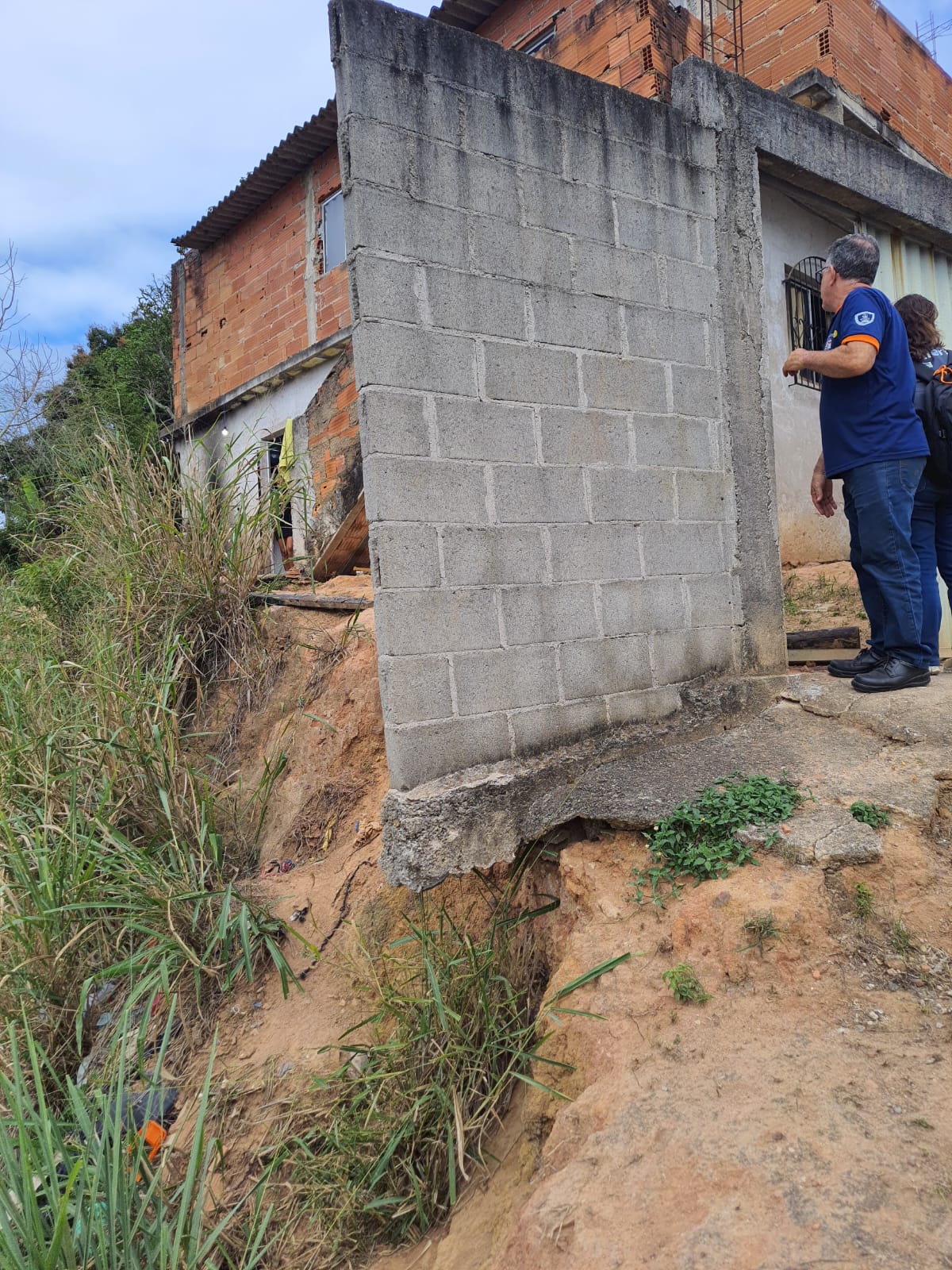 Foto de um técnico visitando uma casa cujo muro está sobre um barrranco