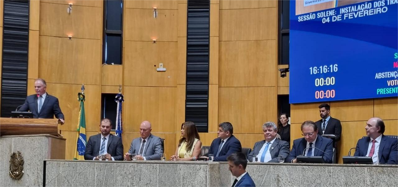 Foto da mesa com a presença de autoridades na sessão solene. No púlpito, o governador discursa