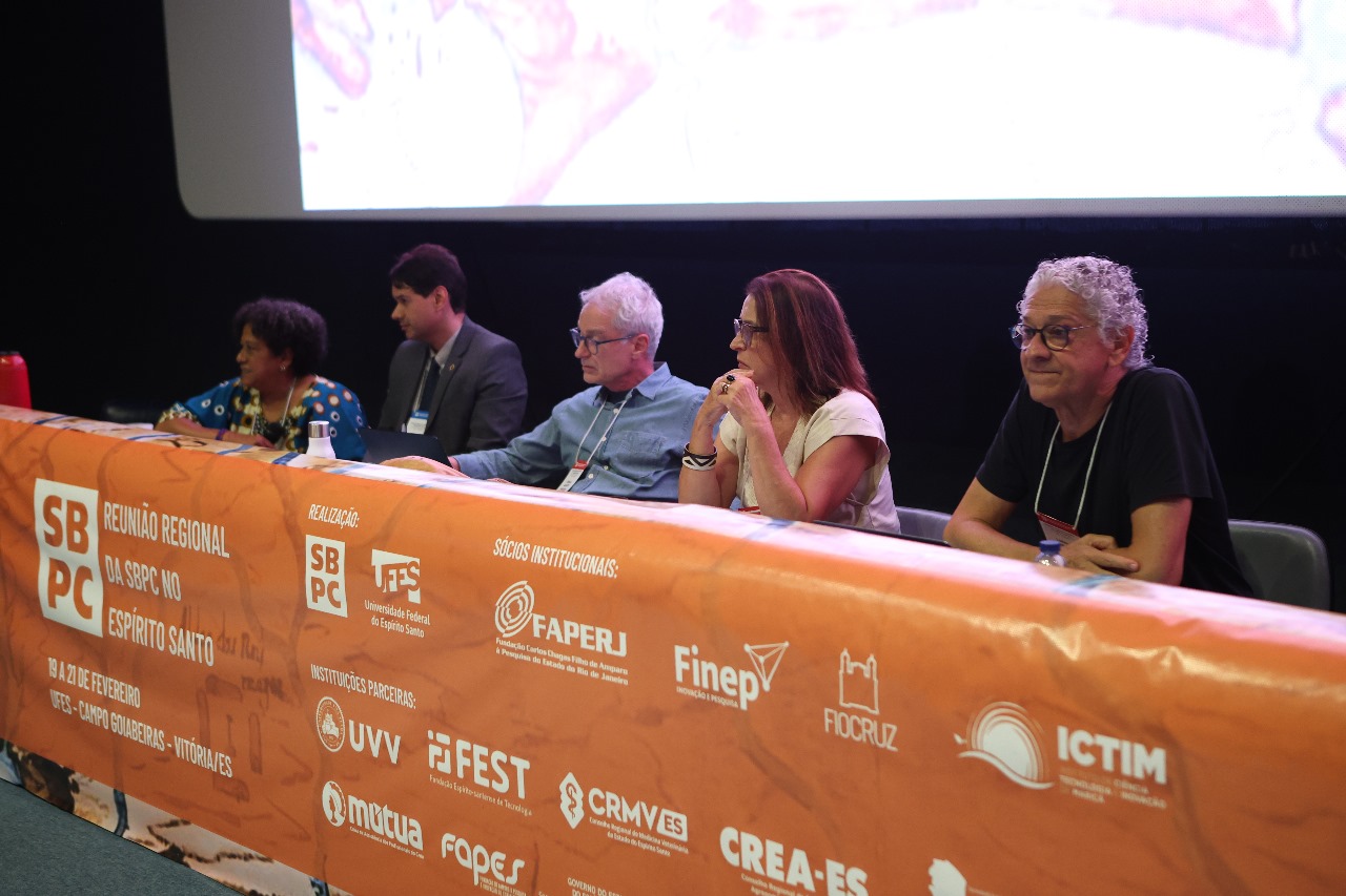 Foto dos palestrantes sentados à mesa principal do evento