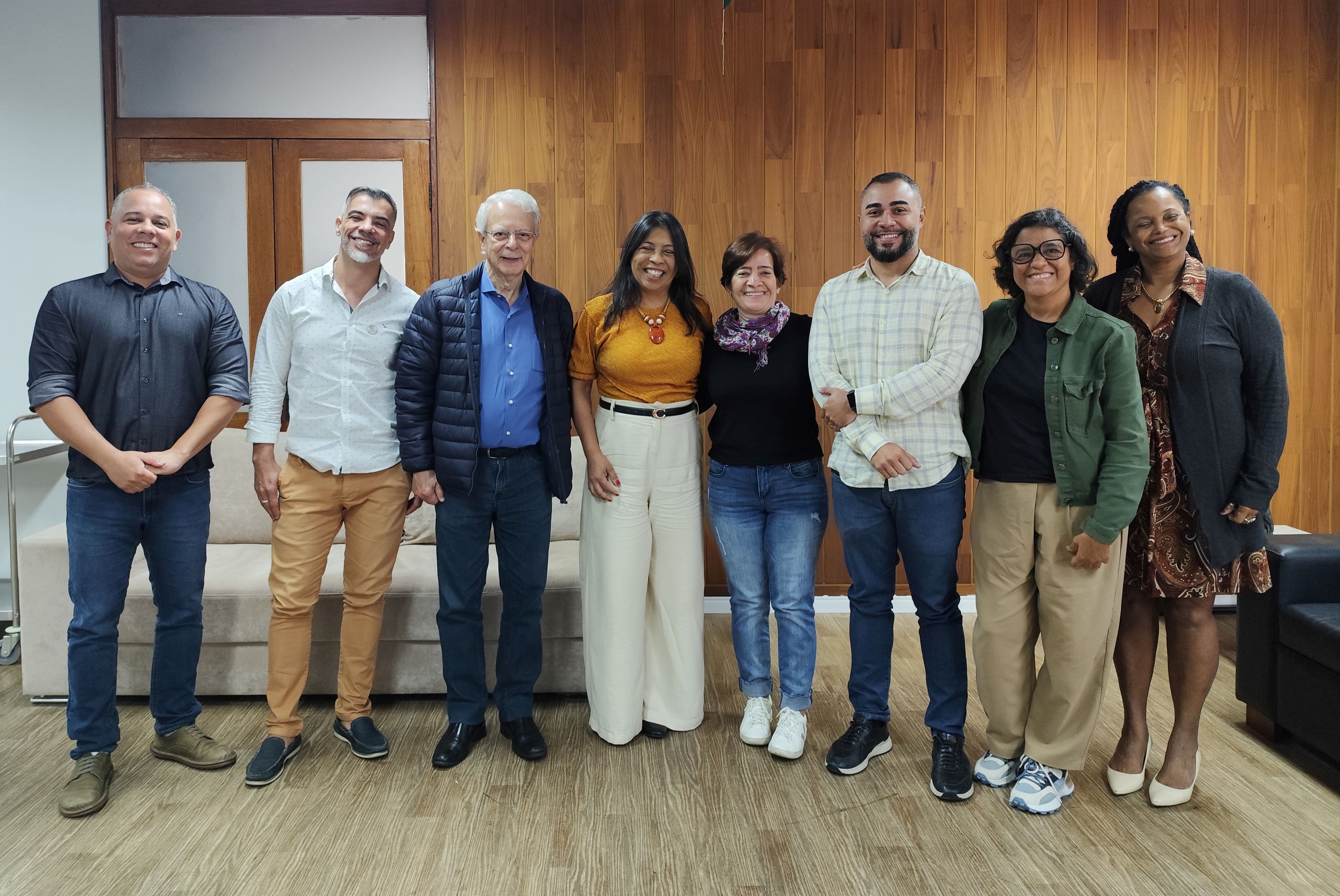 Todos os participantes da reunião em pé, na sala de reuniões, posando para a foto