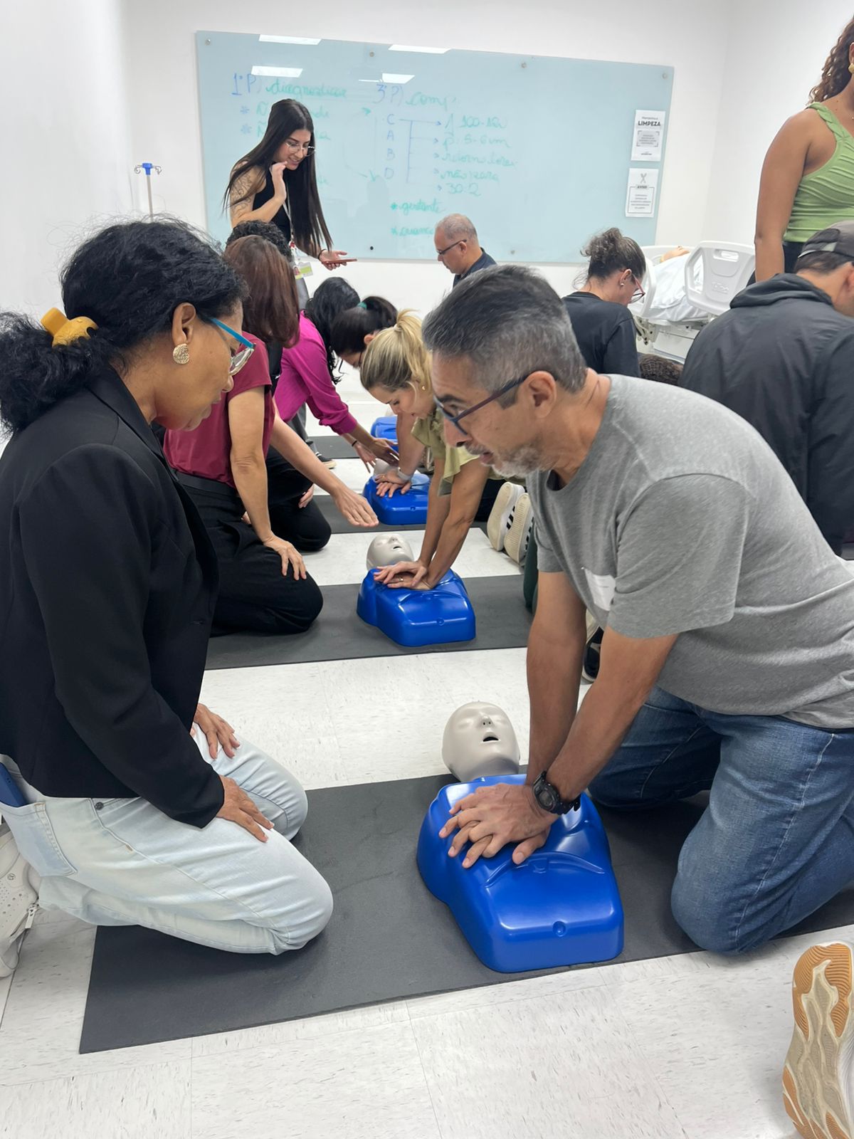 Foto da sala de treinamento, com o professor simulando uma massagem cardíaca em um boneco