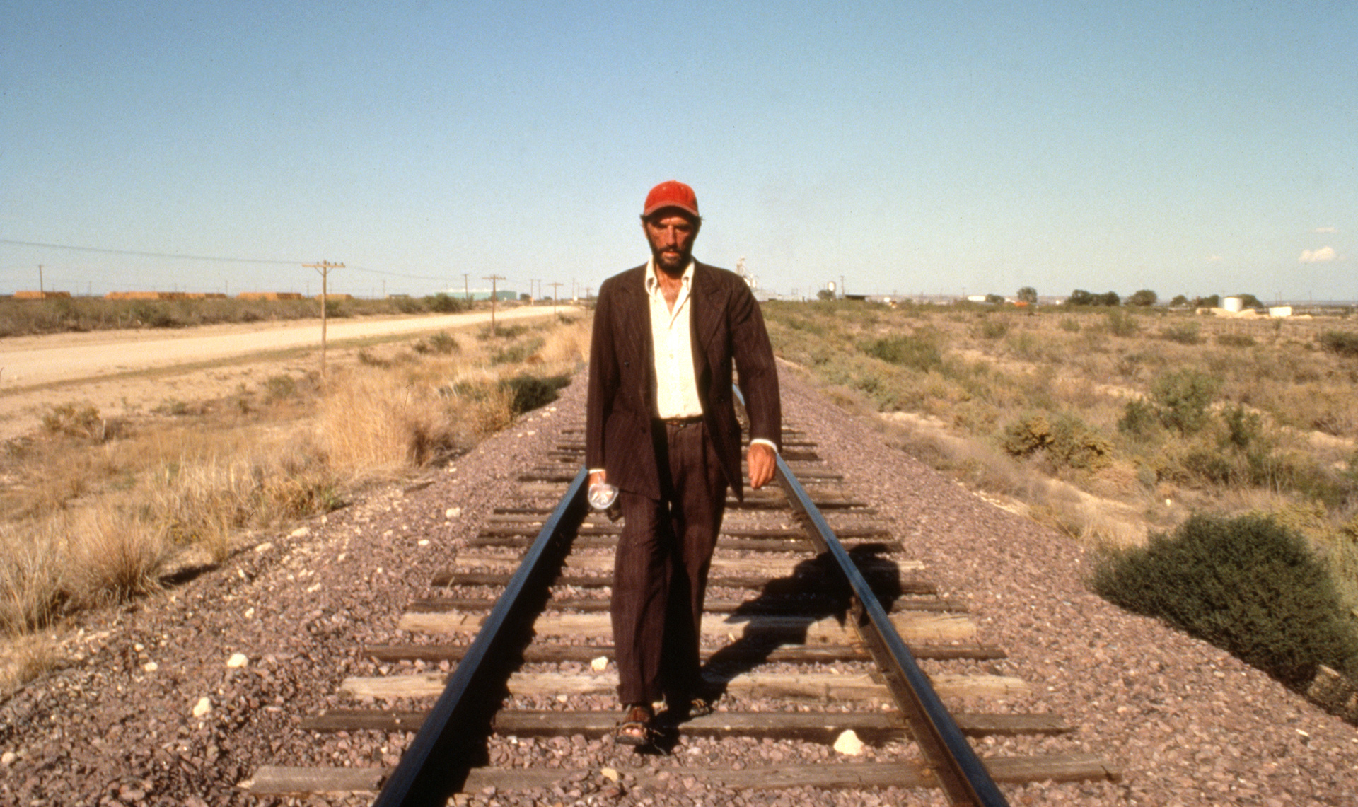 Cena de Paris, Texas, na qual a personagem principal aparece andando sobre trilhos no deserto