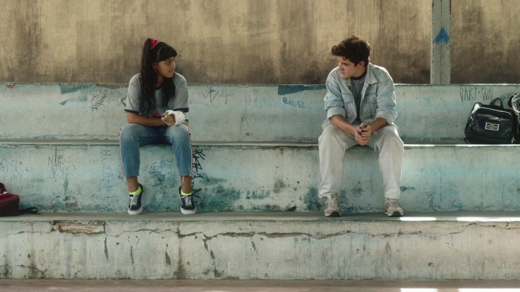 Cena de O Último Episódio no qual aparecem as personagens Erik e Sheila conversando sentados em uma arquibancada