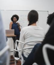 Imagem de uma professora em sala de aula à frente de uma turma de adultos