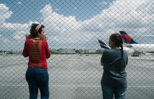 Cena de O Estranho, onde duas moças estão de frente para um alambrado do Aeroporto de Guarulhos