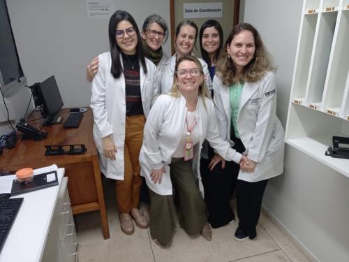 Foto de integrantes do serviço de cuidados paliativos na qual aparecem seis mulheres, de jaleco, em uma sala do hospital, posando para a foto.  