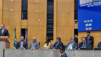 Foto da mesa com a presença de autoridades na sessão solene. No púlpito, o governador discursa