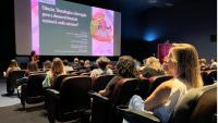 Foto do público assistindo a palestra, com a professora à frente