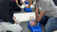 Foto da sala de treinamento, com o professor simulando uma massagem cardíaca em um boneco