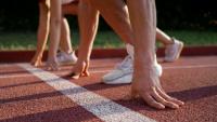 Imagem de mãos e pés de atletas em pista de atletismo, em posição de largada