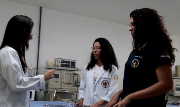 Foto de uma professora ensinando duas alunas do curso de medicina