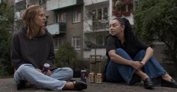 Cena de Erupcja que mostra duas jovens conversando sentadas no chão