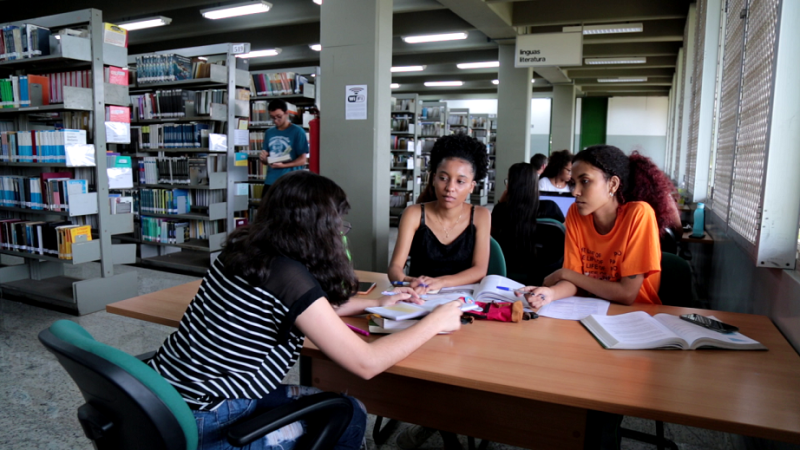 Três mulheres jovens estudando em uma mesa da biblioteca