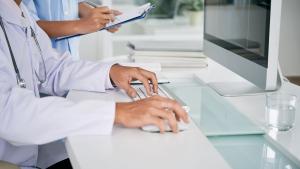 Imagem das mãos de um médico digitando no teclado de um computador